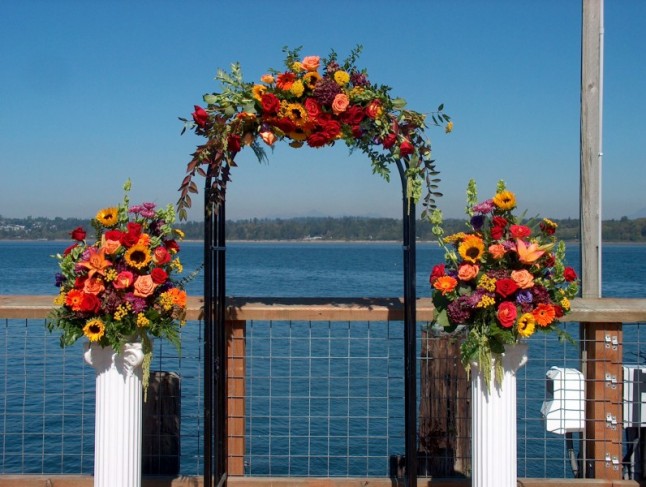 This wedding ceremony arch is decorated with colorful fall flowers that 