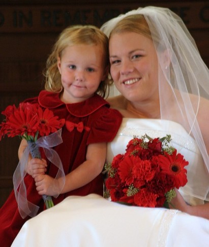 The red gerbera daisies in her handtied bouquet accentuate her dress and