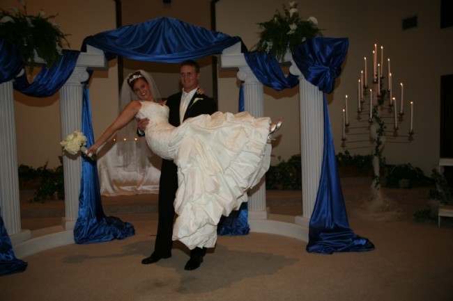  in the air in front of their white and royal blue wedding decorations