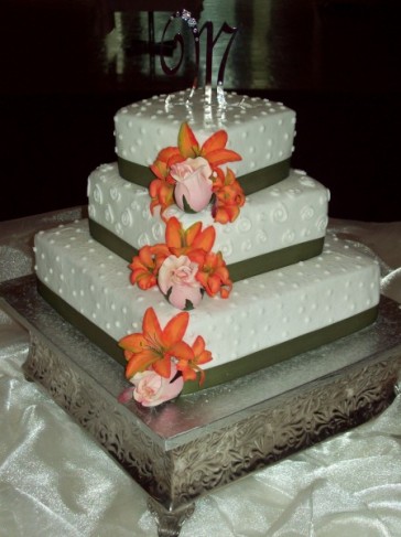 This wedding cake is embellished with pink and orange flowers green ribbon 