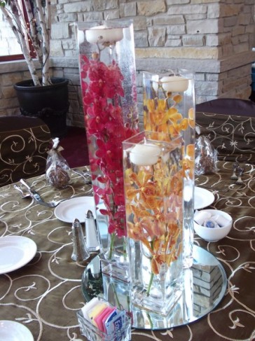 This floral centerpiece shows three vases with red and gold orchids