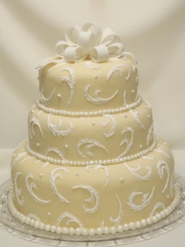 Feathery swirls and shimmery beads and bow on a beige fondant wedding cake
