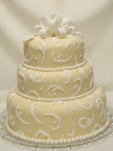 Feathery swirls and shimmery beads and bow on a beige fondant wedding cake 